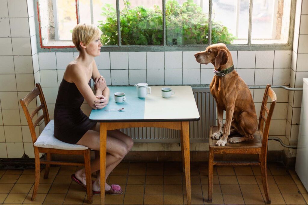 Frau sitzt mit Hund am Frühstückstisch